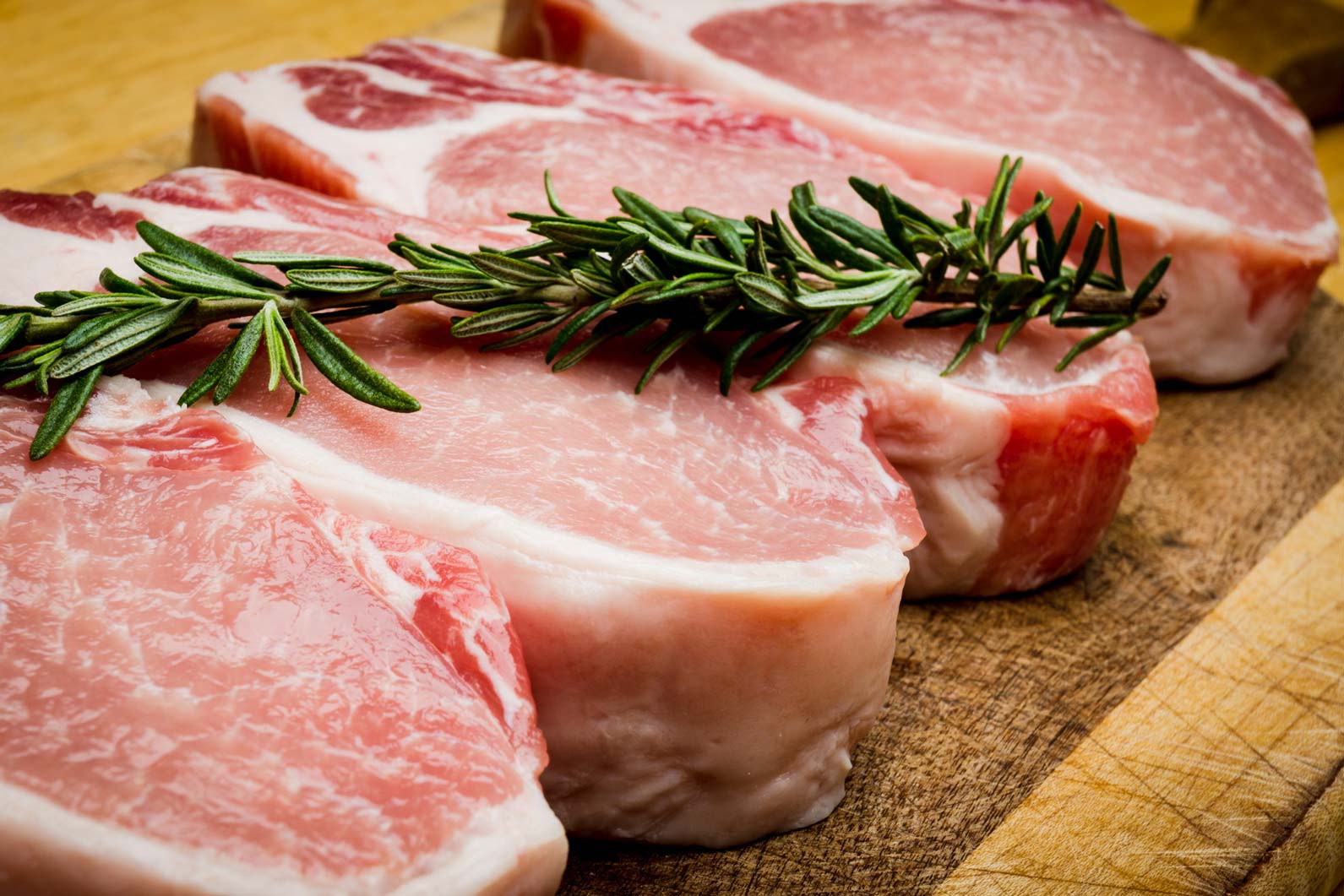 Four marbled pork chops lined up on a cutting board.
